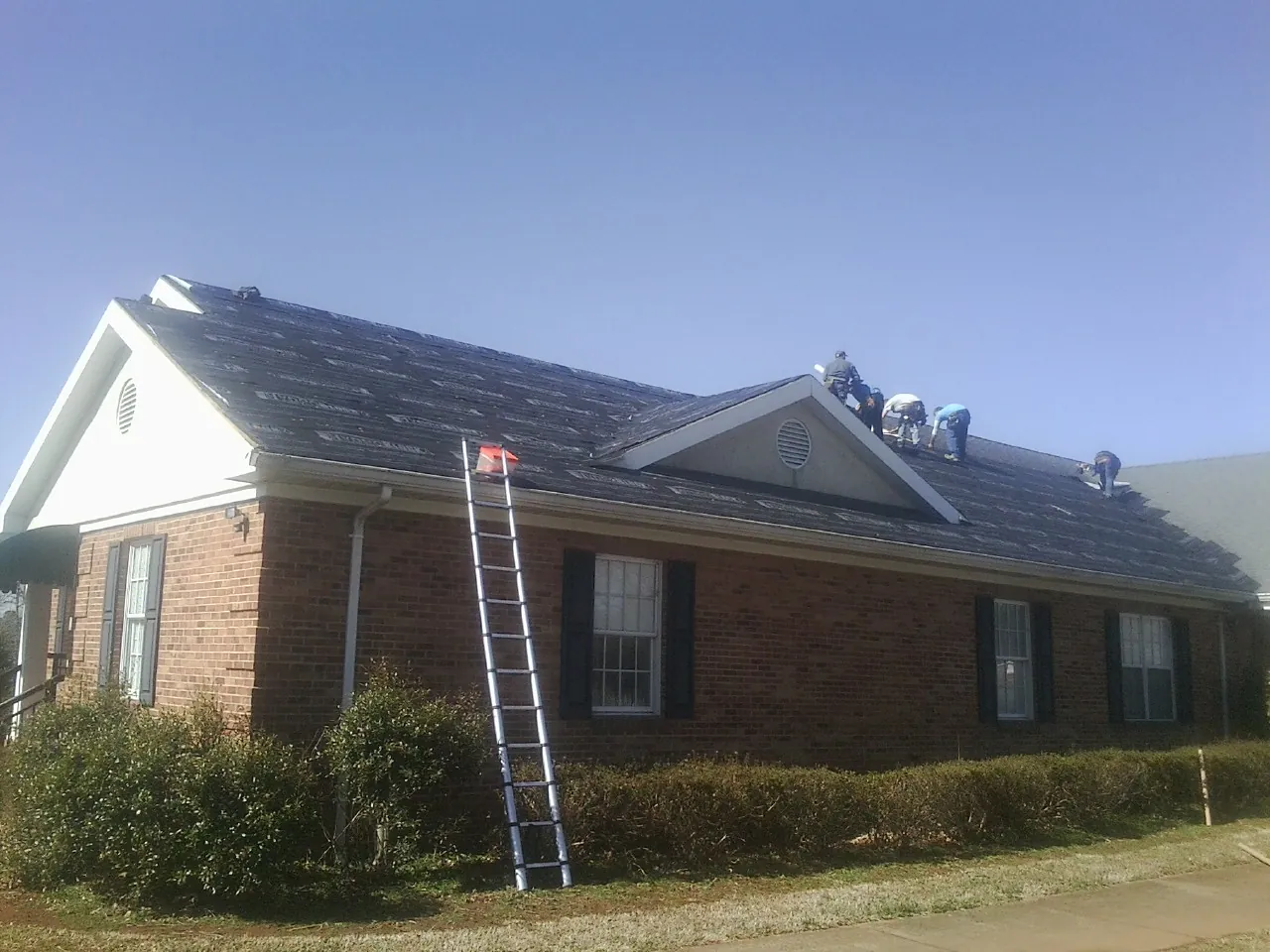 Crew tearing shingles off a brick ranch roof with a ladder set — Emergency Roof Repair work by our crew in Rutherford
