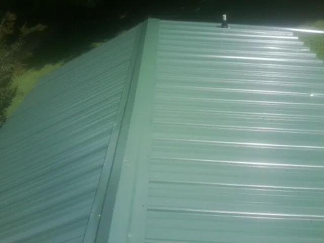 New green metal panels meeting at the ridge of a roof — Flat Roof Repair work by our crew in Rutherford