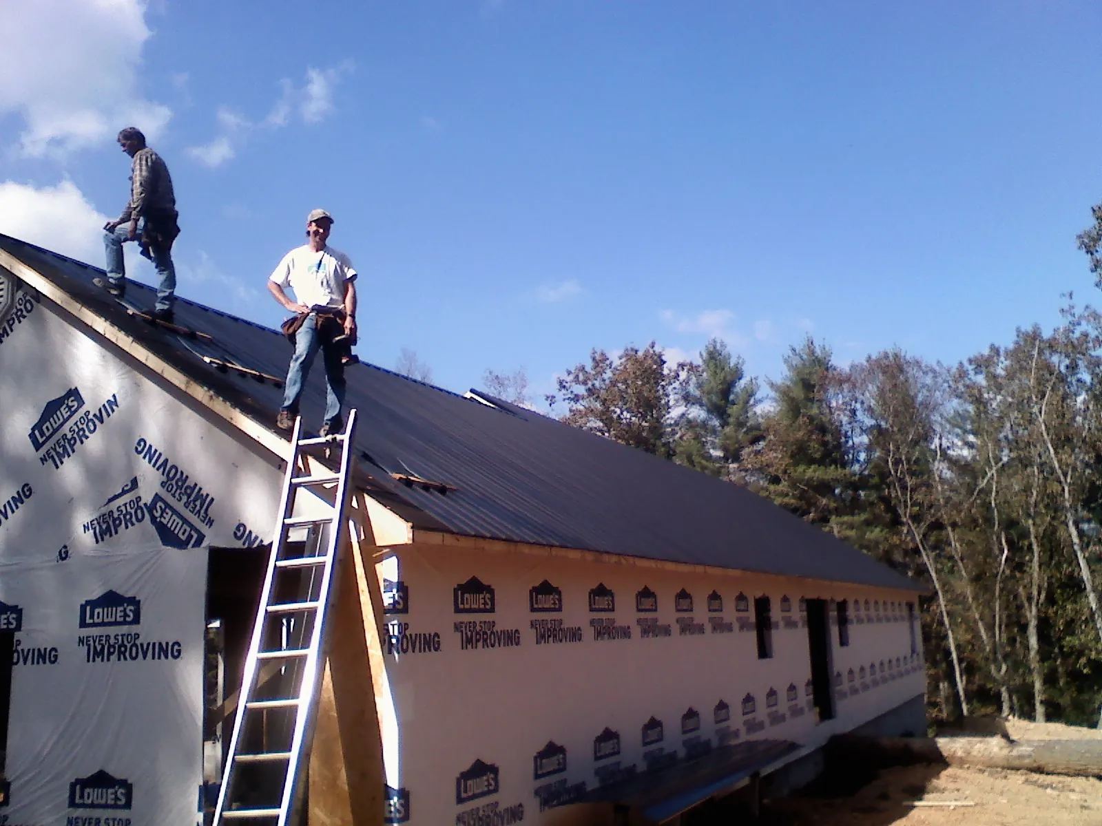 Two roofers standing on a long dark metal roof over a wrapped building in Rutherford