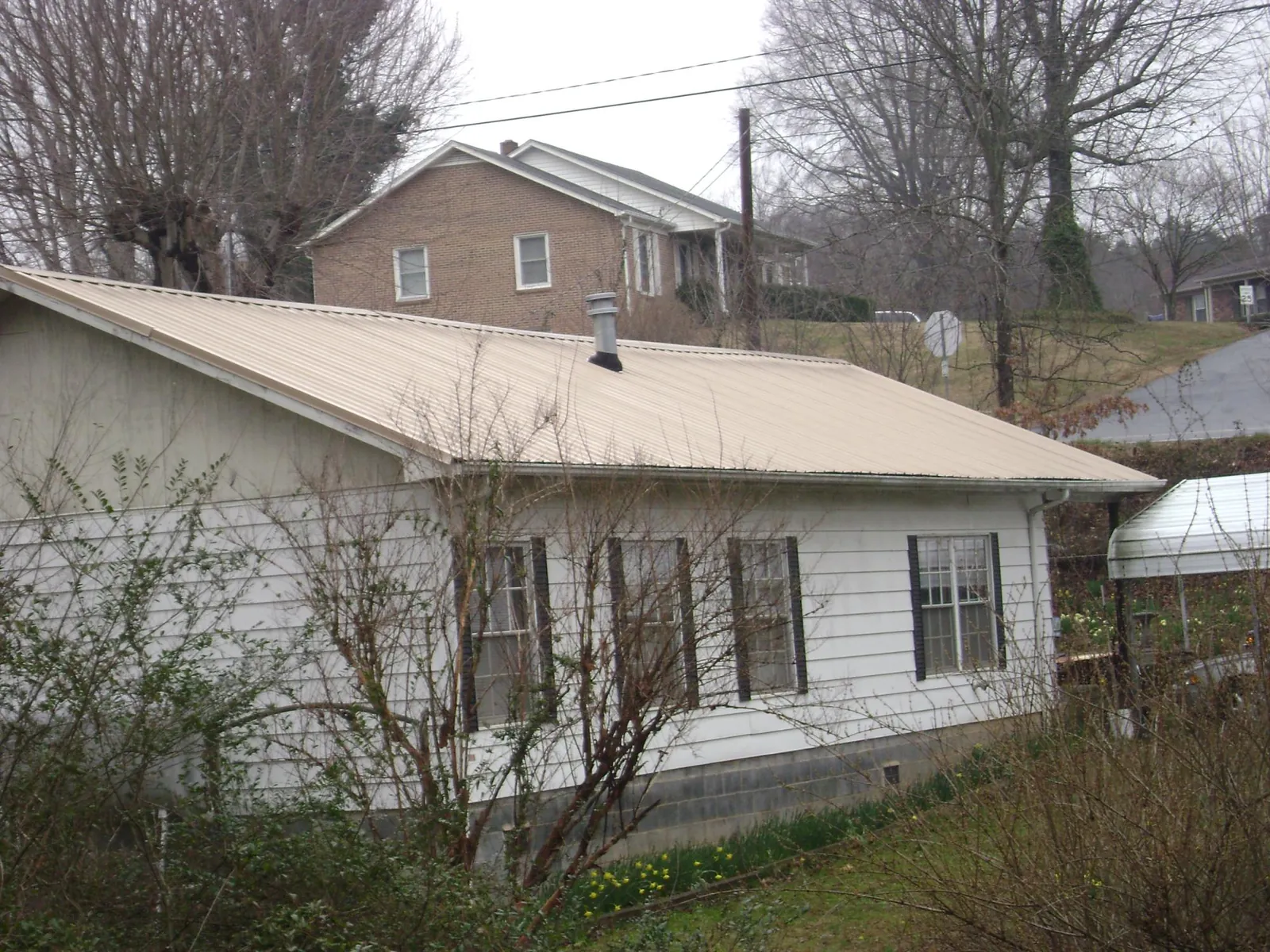 Tan metal roof on a white sided house set into a hillside — Commercial Roofing by Roofing Brothers in Rutherford